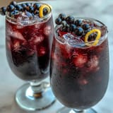 Black Currant and Cassis Cocktail poured over ice cubes with a lemon twist, showcasing its vibrant ruby red hue.