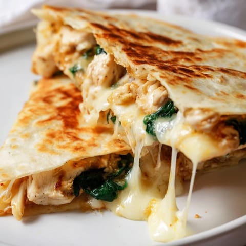 A sizzling Chicken and Spinach Quesadilla being folded in a skillet, with bubbling cheese and a side of fresh salsa and sour cream.