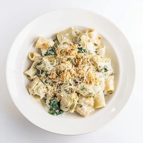 A spoon lifts creamy Parmesan sauce from the vegetarian pasta casserole with spinach.