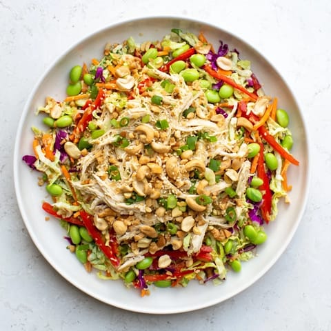 Colorful bowl of Edamame Crunch Chicken Salad with shredded chicken, crisp cabbage, carrots, and edamame tossed in ginger dressing.
