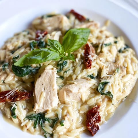 Steaming Tuscan Chicken Orzo with creamy sauce, tender chicken, and vibrant spinach in a rustic skillet.