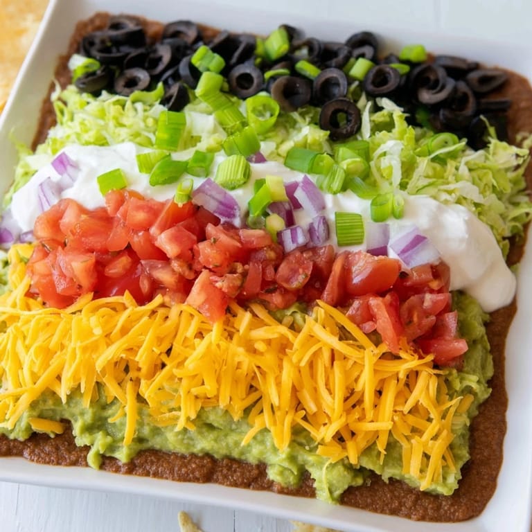 Creamy guacamole atop refried beans in this delicious, layered seven-layer dip appetizer.