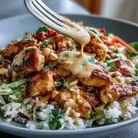 Sautéed chicken and vibrant veggies sit atop coconut rice, drizzled with creamy peanut sauce.