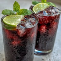 Chilled black currant mocktail garnished with fresh mint and lime slices served over ice in a tall glass.