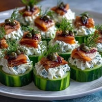 Cucumber Bites with Cream Cheese and Smoked Salmon on a white platter, garnished with capers and dill, perfect for summer parties.